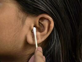 mulher limpa orelha suavemente com fone de ouvido, Cuidado e limpeza foto