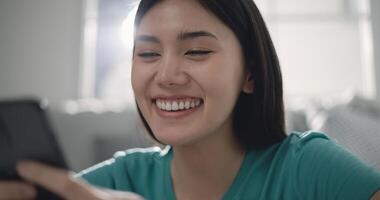 alegre ásia jovem mulher usando Smartphone dentro mão dentro vivo quarto foto