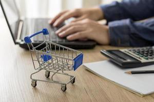 carrinho de compras na mesa de madeira e um homem usando um computador para conversar com o cliente ao fundo foto