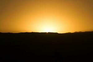 Preto silhueta do a montanhas às pôr do sol com dourado céu foto