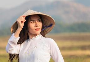 retrato de mulher vietnamita em um vestido branco usando um ao dai caminhando feliz no prado noturno foto