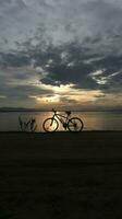 silhueta do uma bicicleta contra a fundo do a pôr do sol em a lago foto