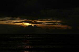 uma nublado céu sobre a oceano com uma Sombrio céu e a Sol configuração atrás isto foto