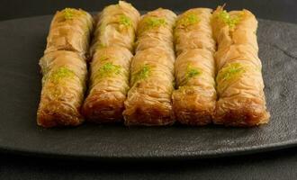 peças do cozido baklava dentro querida e borrifado com pistachios em uma Preto borda foto