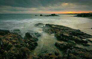 dramático nublado pôr do sol marinha cenário do rochoso costa às selvagem atlântico caminho, algas marinhas de praia dentro município galway, Irlanda foto