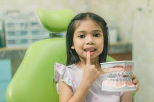 ásia menina dentro dental cadeira, com dente escovar. medicamento, odontologia e cuidados de saúde conceito foto