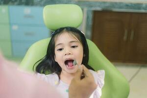 fechar acima retrato do uma caucasiano menina tendo a exame às a pediatra dentista enquanto sorridente às Câmera foto