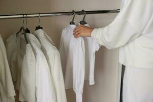 uma menina dentro branco roupas trava luz coisas dentro uma armário de roupa em uma cabide foto