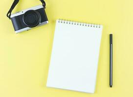 plano deitar do em branco página aberto caderno com caneta e digital Câmera em amarelo fundo com cópia de espaço. foto