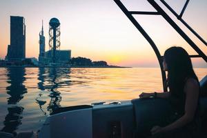 pessoa do sexo feminino senta no barco e olha para a beira-mar de Batumi e atrações famosas com o pôr do sol ao fundo foto