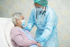 médico asiático usando protetor facial e terno novo normal para verificar paciente proteger segurança infecção covid 19 surto de coronavírus na enfermaria de quarentena do hospital foto