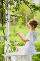 jovem noiva loira com lingerie branca usando perfume em um balanço de corda foto