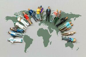 miniatura pessoas em pé em a mundo mapa com cinzento fundo foto