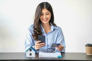 ásia mulher com grandes cabelo dentro a azul camisa é usando uma crédito cartão para comprando uma Novo casa e olhando às compra de casa documentos a idéia do compra uma casa com uma crédito cartão. foto