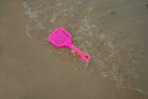 Rosa brinquedo plástico pá em de praia areia e ondas. conceito foto para verão Tempo