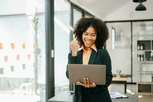 confiante o negócio especialista atraente sorridente jovem mulher digitando computador portátil ang segurando digital tábua em escrivaninha dentro escritório. foto