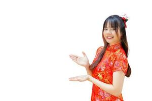 linda garota asiática com cabelos longos que usa um vestido cheongsam vermelho no tema do ano novo chinês enquanto ela mostra a mão para apresentar algo em um fundo vermelho. foto
