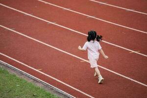 bebê ásia menina corre corrida às corrida acompanhar, corrida campo às estádio. pequeno menina corrida às pôr do sol feliz bebê menina sorridente. pequeno menina corrida às pôr do sol. fofa bebê menina corrida às corrida acompanhar. foto