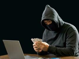 hacker espião homem vestindo uma Preto camisa, sentado em uma cadeira e uma mesa, é uma ladrão, mãos segurando dinheiro, contando a montante obtido a partir de sequestro ou roubando, dentro uma breu sala. foto