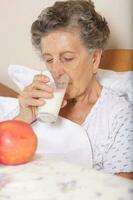 velho mulher bebidas alguns leite dentro a manhã foto