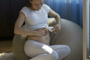 jovem grávida senhora coloca creme em barriga pele foto