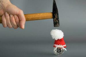 bitcoin dentro uma santa claus chapéu e uma martelo em uma cinzento superfície. foto