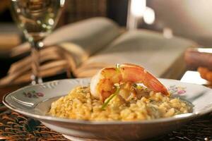 lindo prato do camarão risoto com branco vinho. dentro a fundo velho livros foto