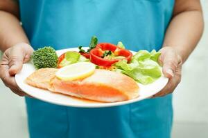 médico segurando salmão estaca e vegetal salada para saudável Comida dentro hospital. foto