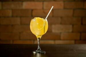 vidro do laranja Caipirinha beber em topo do mesa dentro frente do uma tijolo parede com texto espaço foto