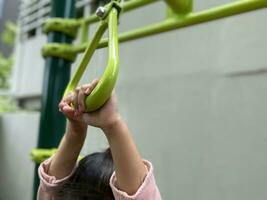 mãos do menina suspensão às Parque infantil. foto