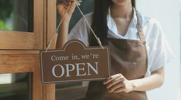 bem-vinda. abrir. barista, garçonete mulher girando aberto placa borda em vidro porta dentro moderno cafeteria café fazer compras pronto para serviço, cafeteria restaurante, varejo loja, pequeno o negócio proprietário, Comida e beber conceito foto