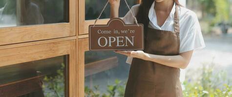 bem-vinda. abrir. barista, garçonete mulher girando aberto placa borda em vidro porta dentro moderno cafeteria café fazer compras pronto para serviço, cafeteria restaurante, varejo loja, pequeno o negócio proprietário, Comida e beber conceito foto