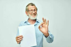 velho homem dentro uma azul camisa e óculos uma branco Folha do papel luz fundo foto