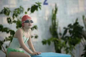 uma menina dentro uma roupa de banho e uma natação boné com óculos dentro a Esportes piscina. foto