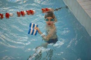 Garoto dentro uma natação boné e natação óculos dentro a piscina. a criança é acionado dentro a natação seção. foto