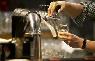 mulher garçom derrama Cerveja para dentro uma vidro às a bar. foto