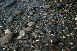 molhado pequeno pedras dentro água do mar fechar-se. seixo de praia foto