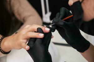 manicure serviço. fechar-se. aplicando unha polonês com uma fino escovar, nivelamento a superfície. a manicuro tintas dela unhas com uma transparente gel polonês. bem cuidado unhas. foto