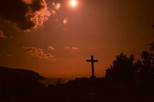 tarde panorama. a Cruz do Deus em a Colina dentro nublado clima. uma cenário em uma caloroso laranja pôr do sol dia. foto