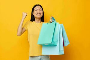 encantador jovem ásia mulher dentro uma amarelo camiseta com multicolorido compras bolsas estúdio modelo inalterado foto