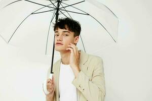 agradável jovem cara com a aberto guarda-chuva dentro uma terno luz fundo foto