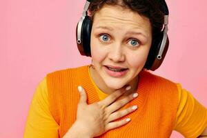 lindo mulher ouvindo para música com fones de ouvido laranja suéter emoções Diversão cortada Visão inalterado foto