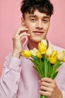 bonita homem dentro uma Rosa camisa com uma ramalhete do flores gesticulando com dele mãos Rosa fundo inalterado foto
