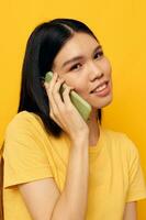 retrato ásia lindo jovem mulher comunica em a telefone emoções amarelo fundo inalterado foto