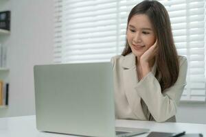 trabalhando mulher, retrato do sorridente Ásia menina dentro trabalhos roupas usando computador portátil, sentar às escritório e fazendo pesquisar, cópia de espaço, feliz alegre fofa negócios, positivo energia, o negócio plano, fêmea executivo foto