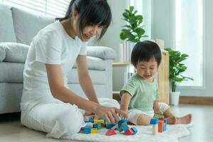 feliz Ásia mãe jogar e aprender brinquedo blocos com a pequeno garota. engraçado família é feliz e animado dentro a casa. mãe e filha tendo Diversão gastos Tempo junto. feriado, atividade, desenvolvimento foto