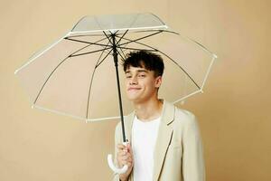uma homem com a aberto guarda-chuva dentro uma Jaqueta proteção a partir de a chuva bege fundo foto