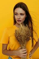 lindo menina dentro amarelo Camisetas, seco flores dentro mãos isolado fundo foto
