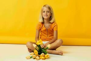 pequeno menina sentado em a chão com uma ramalhete do amarelo flores Diversão amarelo fundo foto