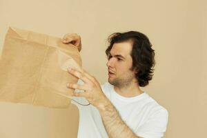 alegre homem dentro uma branco camiseta com papel saco bege fundo foto